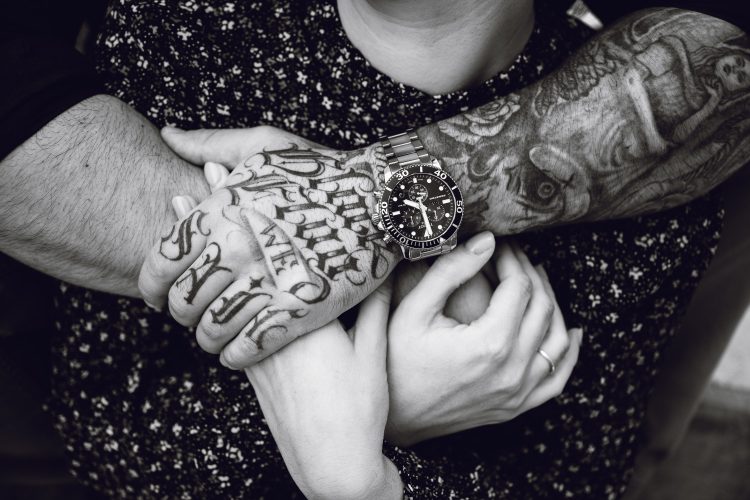 routscher_Roger_Nebiker_fotograf_paarshooting_baselland_burg_ruine_farnsburg_Tätowierter Mann umarmt seine Verlobte. Handtattoos.